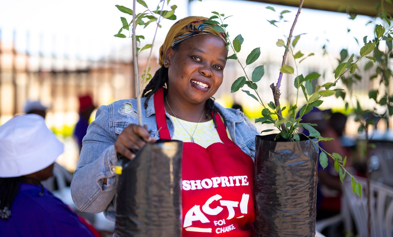 A woman holding two trees in a red Shoprite Act for Change apron.