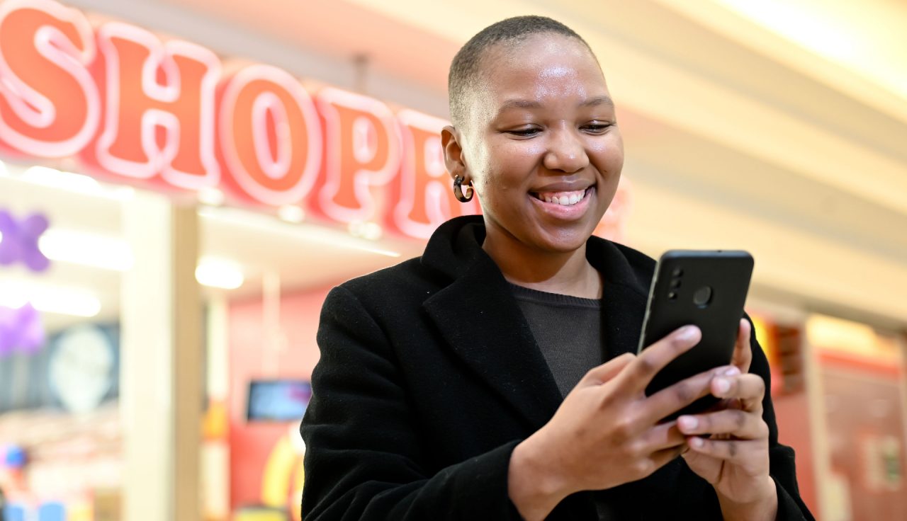 A young lady looking at her phone outside a Shoprite store.